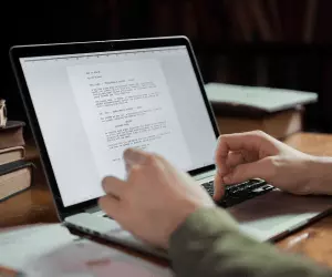 A person writing a cover letter on a laptop wearing a green shirt