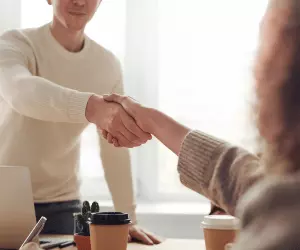 A man about to stand up from a table shaking hands with a female interviewer at the end of the interview