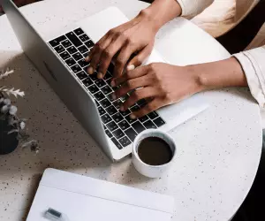 a person typing on their laptop with a coffee sat next to them