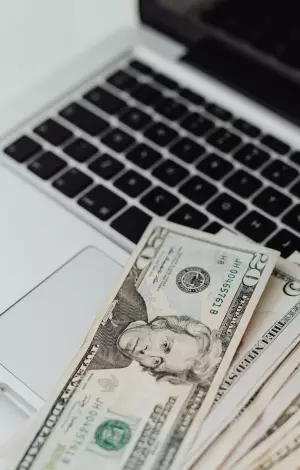 A laptop open with dollar notes sat on the keyboard