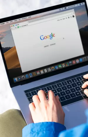 A person on their laptop typing into Google search bar