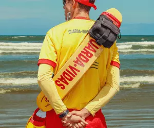 A lifeguard wearing a yellow and red shirt stood on a beach ready to save someones life