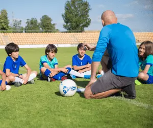 A group of young children sat on a grass field listening to their sports coach