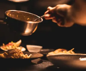 A close up of a chef serving up some food on a plate