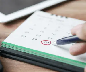 A close up of a calendar and a person pointing to a specific date with a pen to show a deadline
