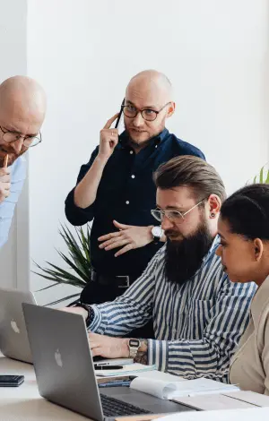 A close up of a group of people working on a project looking at a laptop in an office