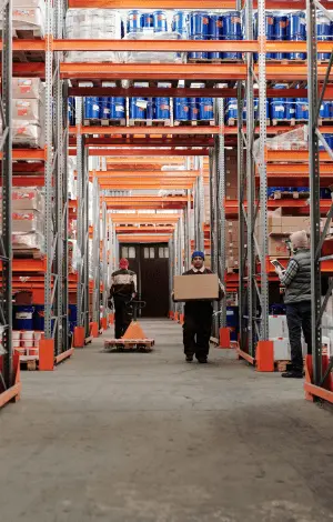 A busy warehouse interior with several people walking and interacting among shelves and storage areas