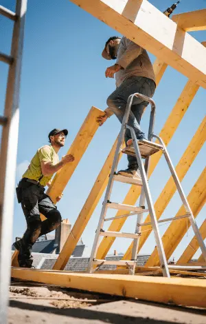 Two men installing wooden beams on a roof, focused on their work in a construction setting.