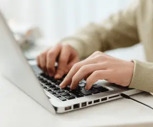 A close up of a woman sat a desk writing a blog on her laptop