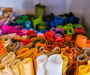 A large pile of vibrant fabrics rolled up in various colours stacked together, showcasing textiles