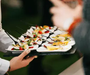 A close up of a waiter holding a tray of canopies at an event, giving them to customers