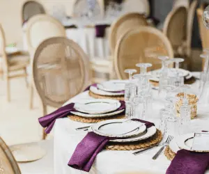 A dining table set with purple napkins and white plates, creating an elegant and colourful table setting at an event