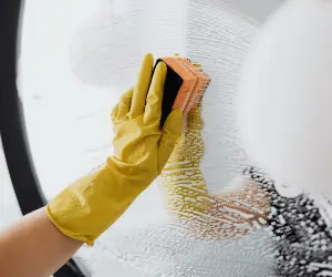 A woman wearing yellow cleaning gloves cleaning a mirror