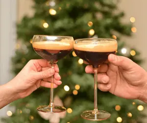 Two people toasting their drinks in front of a Christmas tree at a Christmas party
