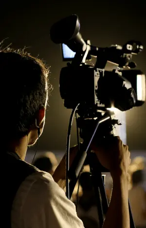 A behind shot of a male photography in a dark studio filming a scene, showcasing media jobs