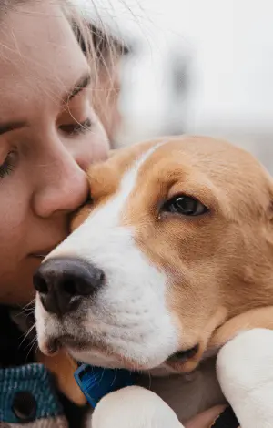 A close up of a girl holding a dog close to her face giving him a kiss