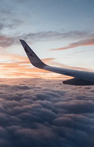 A close-up view of an airplane wing soaring above soft, white clouds under a bright blue sky