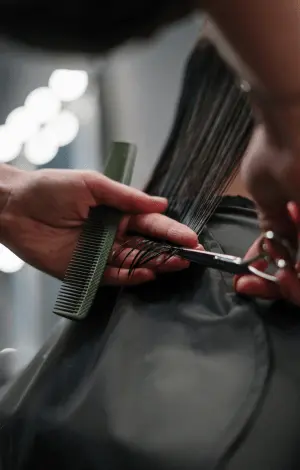 A woman sitting in a salon chair while a stylist cuts her hair