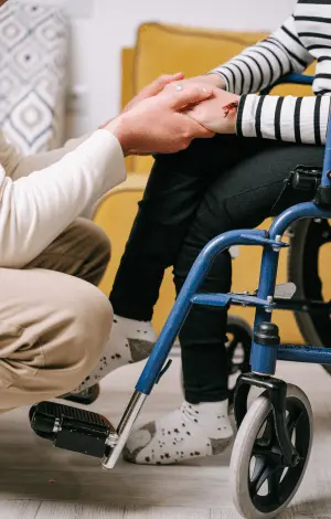 A man holding a woman's hand who is sat in a wheel chair, showing care and attention