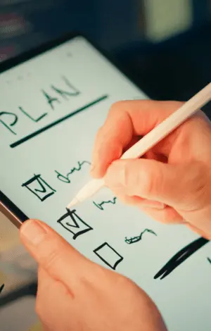 A person holding an ipad writing a plan and ticking off to do's