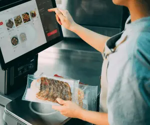A young girl working behind a till as a cashier scanning an item of food