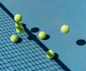 Lots of green tennis balls laying on a blue tennis court