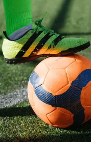 A close up of a football on a pitch with a player resting their foot on top of it