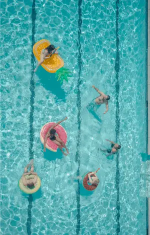 A birds eye view of people relaxing on colourful inflatable toys while floating in a sunny swimming pool
