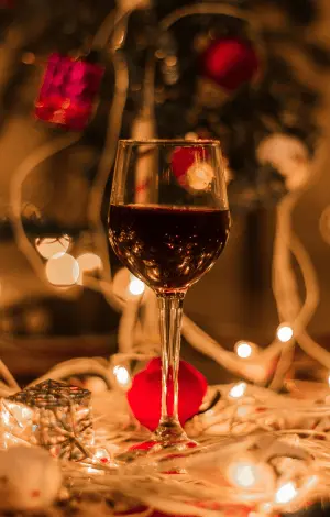 A close up of a wine glass on a table with fairy lights and Christmas decor surrounding it