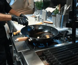 A close up of a person wearing gloves and a black apron cooking on a stove