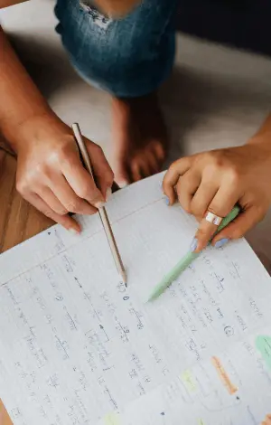 A birds eye view of two people sat at a table both holding a pencil working on studying